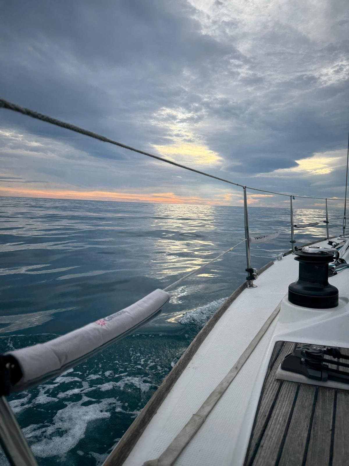Cubierta de un velero navegando en mar abierto bajo un cielo de nubes al atardecer