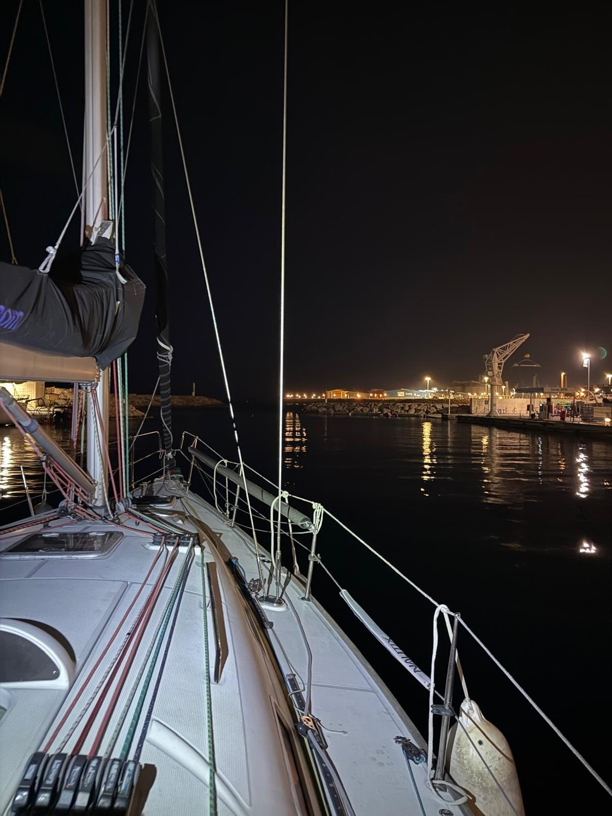 Velero amarrado de noche con las luces del puerto reflejadas en el agua