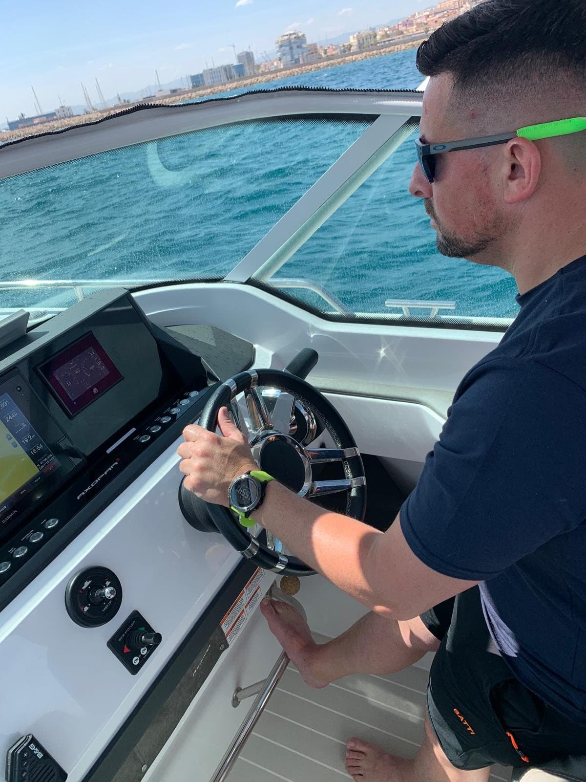 Sergio al timón de una lancha, con gafas de sol y el puerto al fondo